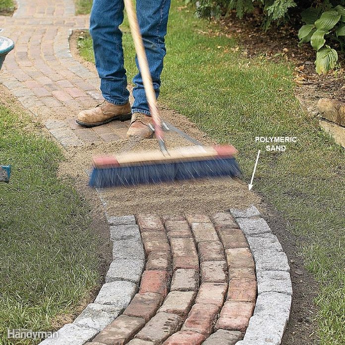 man sweeps sand along brick path