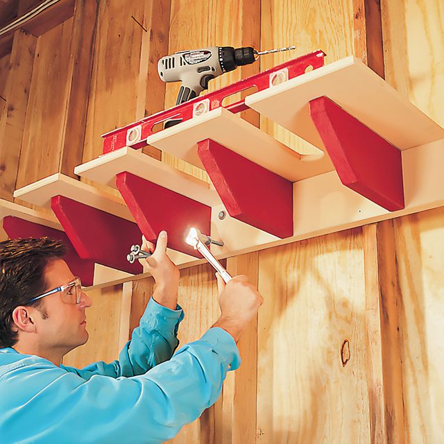 A Man Installing Shovel Rack Against Wooden Wall