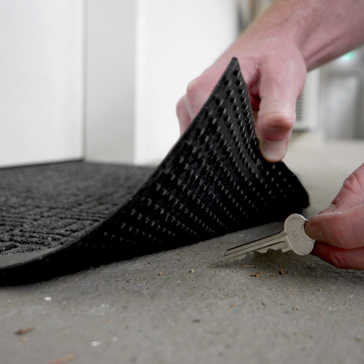 hands retrieving a hidden key from under a mat