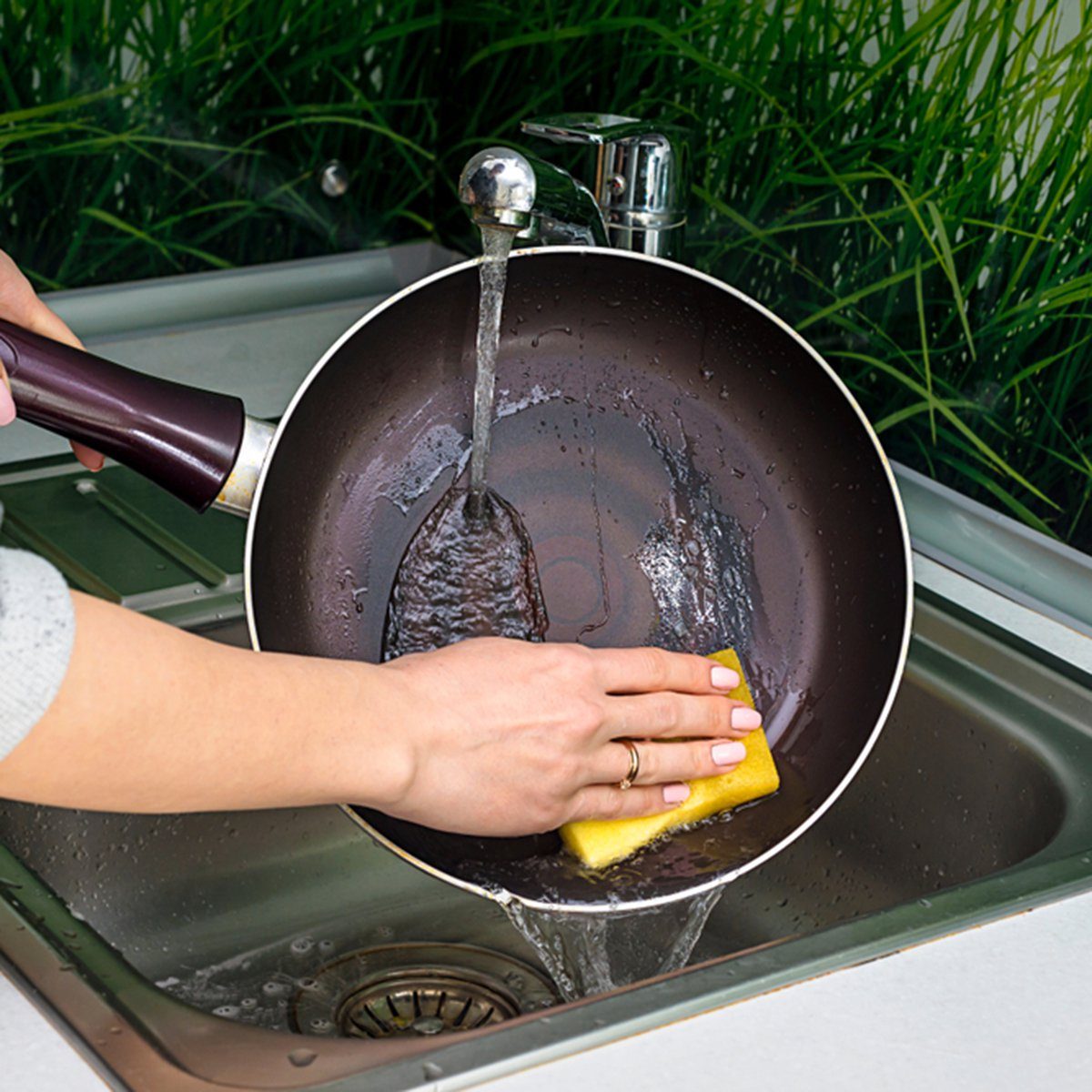 Female hand washing frying pan close up under running water, Young housewife woman washing griddle in a kitchen sink with a yellow sponge, Hand cleaning, manually, by hand, housework dishwasher,; Shutterstock ID 1079775416; Job (TFH, TOH, RD, BNB, CWM, CM): TOH