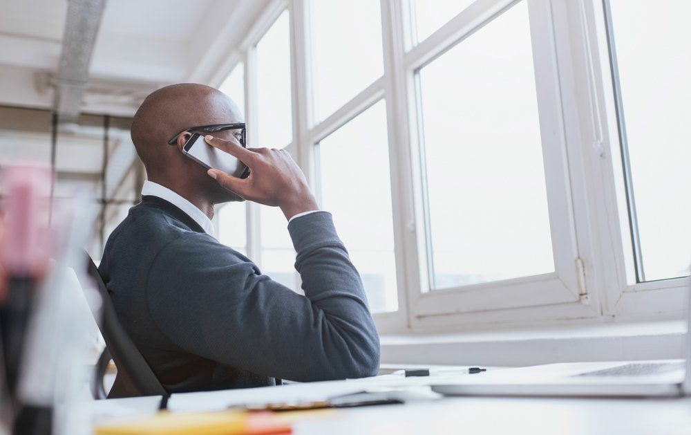 Young african man sitting at his desk talking on his mobile phone in office. African executive using cell phone while at work.