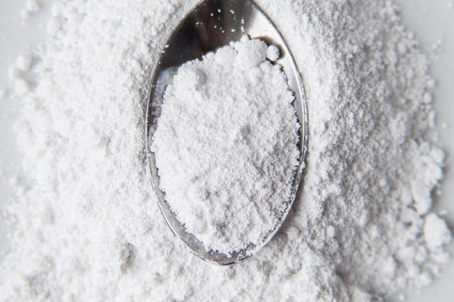 White powder in silver spoon over white background. Top view. Detailed close-up shot. Icing, caster, confectioners or powder sugar pile.