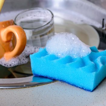 Cleaning the dirty dishes with a blue sponge with detergent in a sink