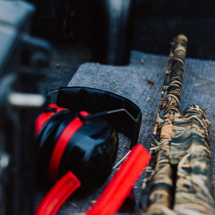 Camo rifle sitting in the back of a truck with other gun accessories for skeet shooting.
