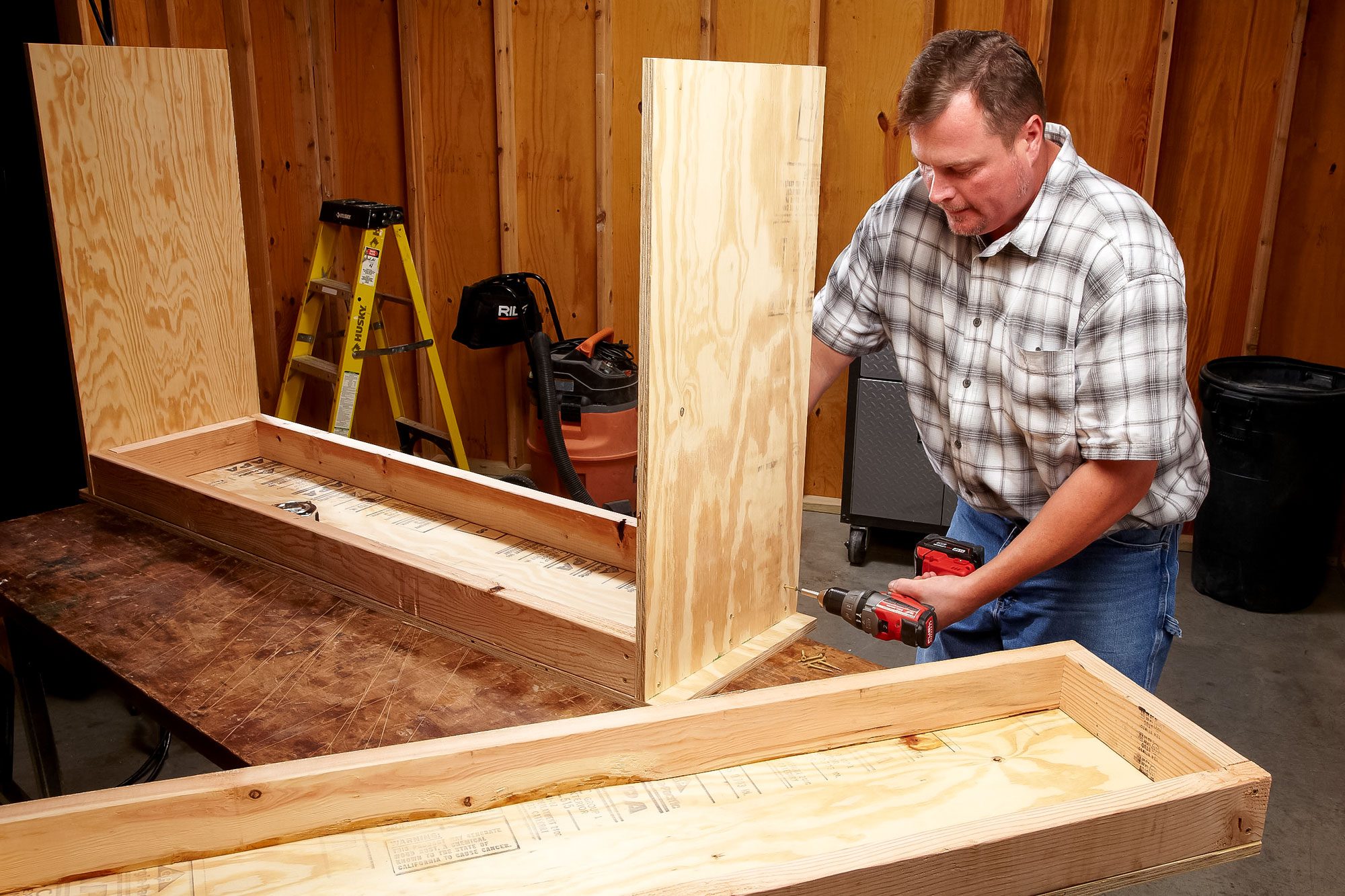 A Man Fastens Screw into Wood with Drill