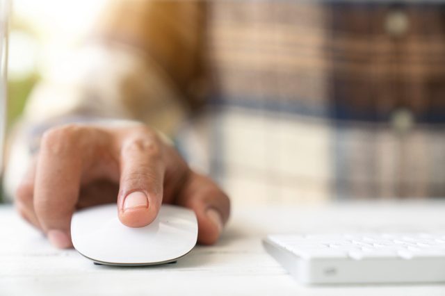 Male hand holding computer mouse with laptop keyboard in the background