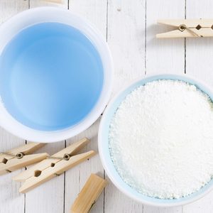 washing liquid and detergent powder with bamboo clothes pins on white wooden
