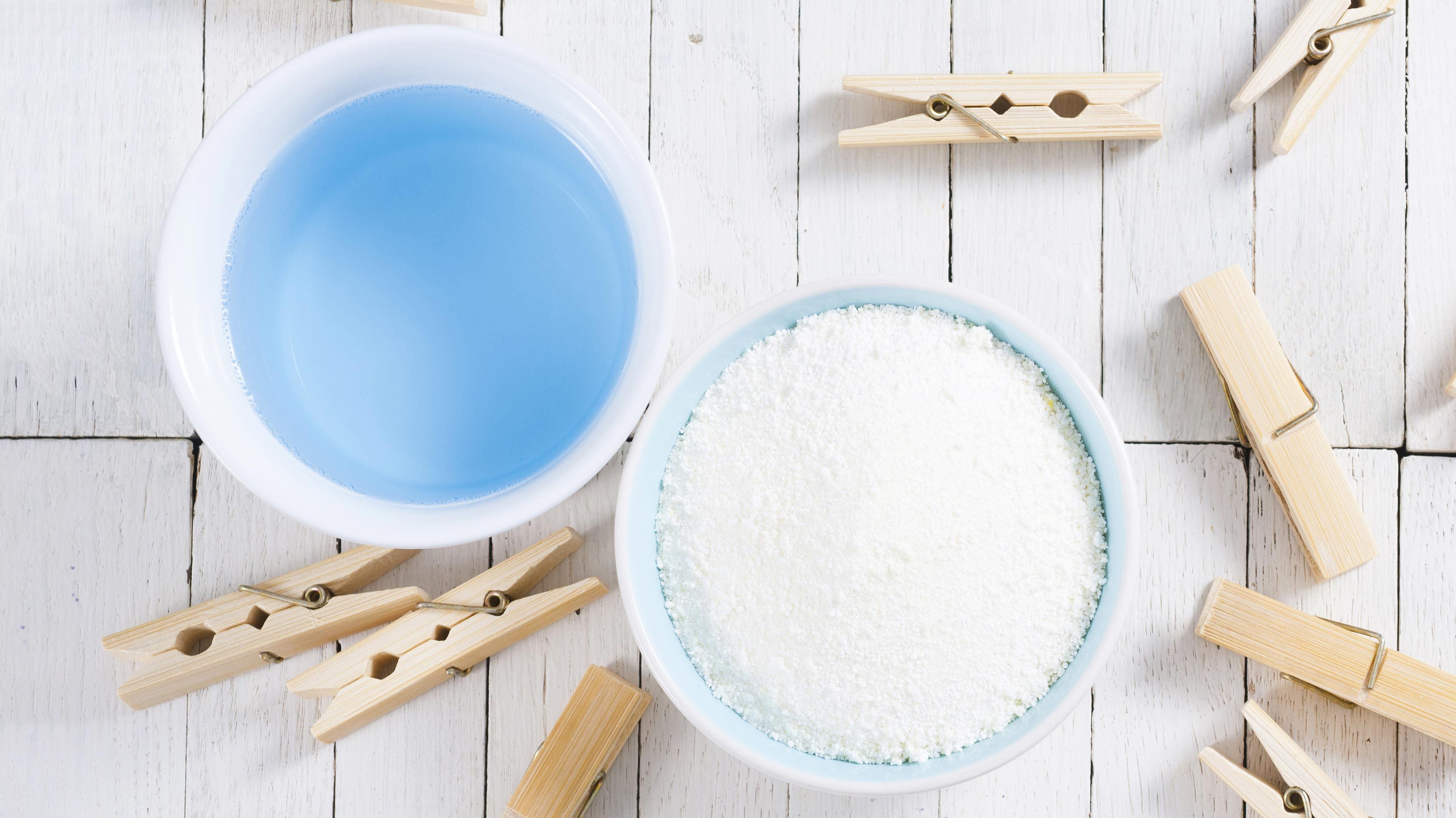 washing liquid and detergent powder with bamboo clothes pins on white wooden