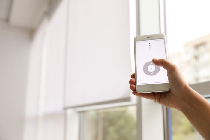 Woman using smart home application on phone to control window blinds indoors, closeup. Space for text