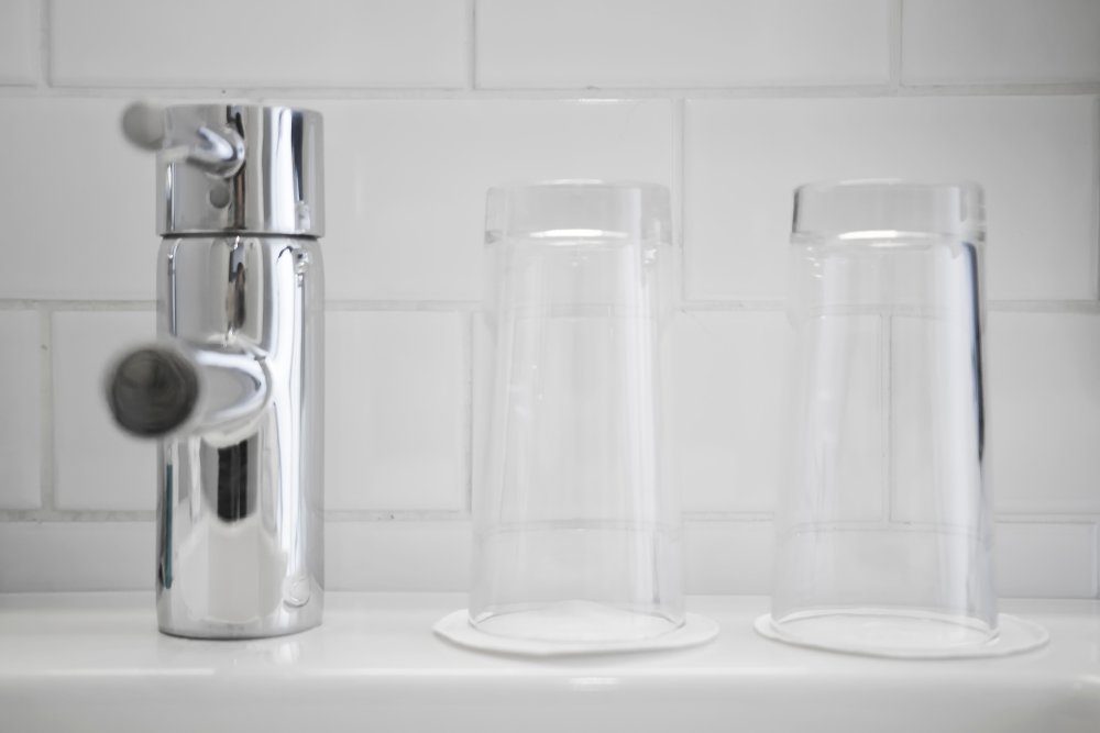 Mixer tap and two clean water glasses in the white bathroom.