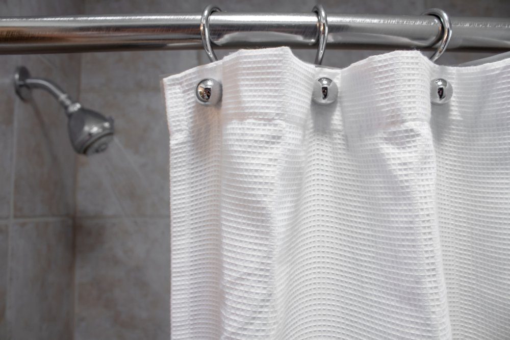 a white shower curtain in an empty shower with water OFF closeup shot