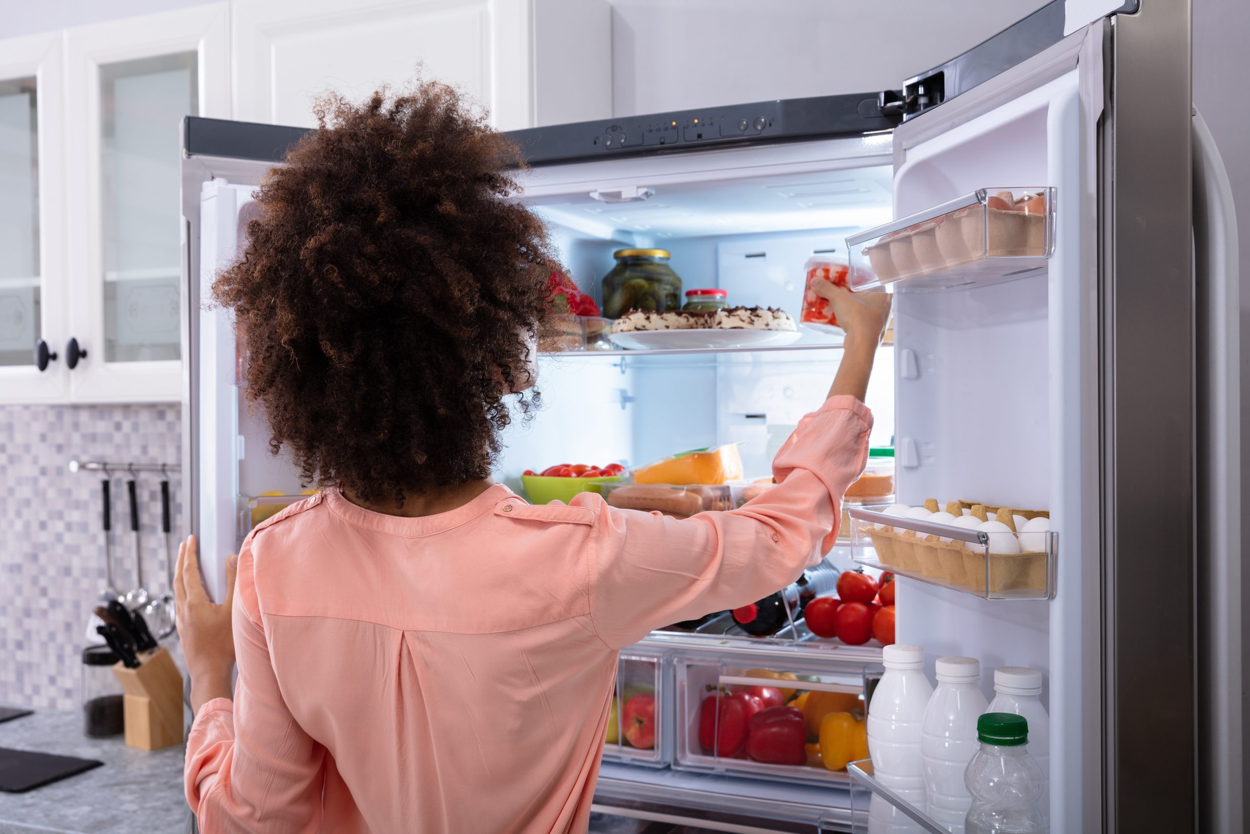 Rear View Of A Young Woman Taking Food To Eat From Refrigerator