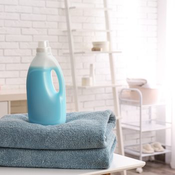 Bottle of detergent and clean towels on table indoors, space for text. Laundry day