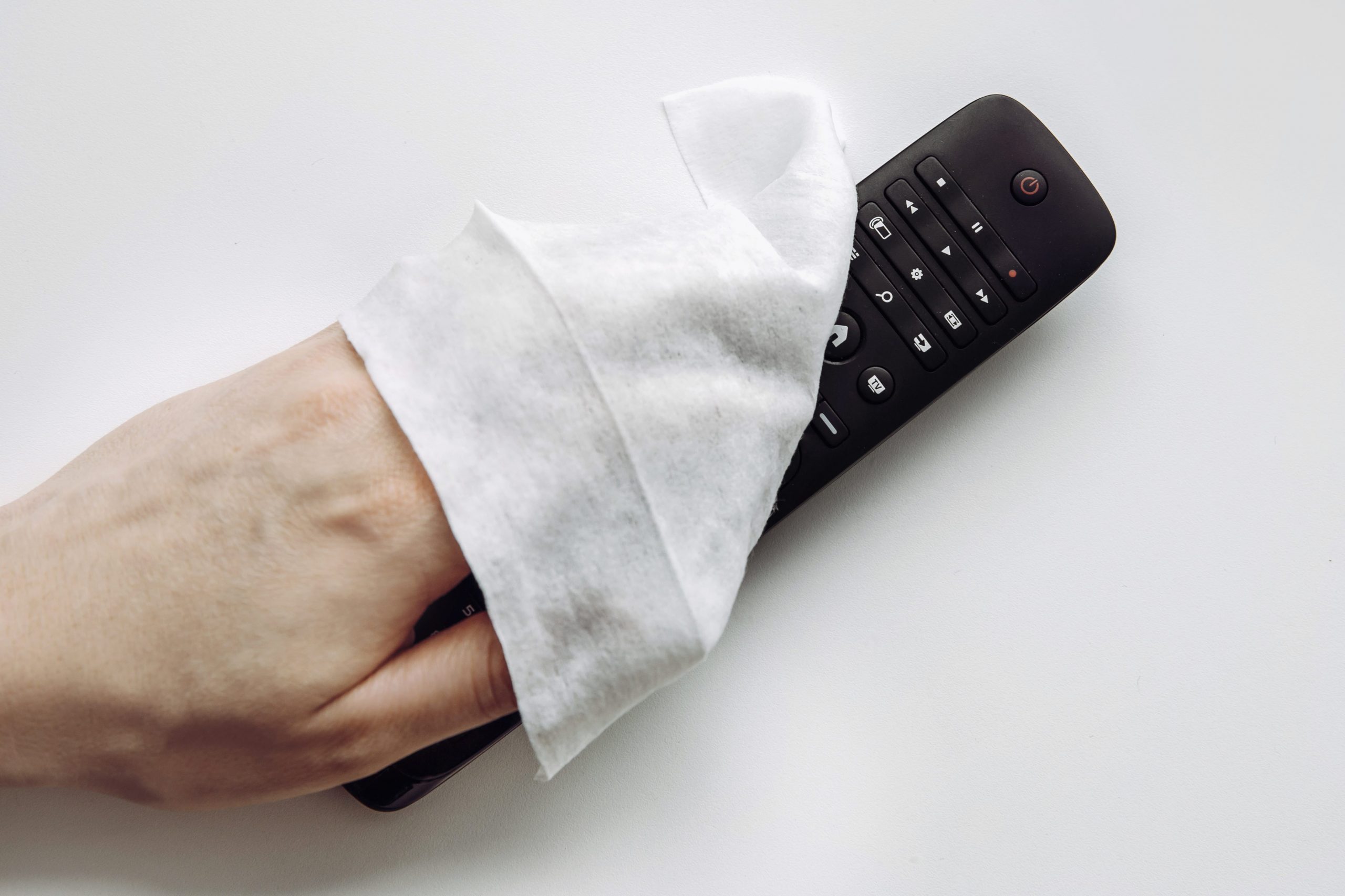 Close up view of man hand using antibacterial wet wipe for disinfecting home TV remote control.