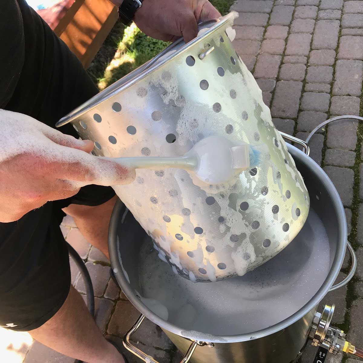 Hands scrubbing an outdoor deep fryer with a brush