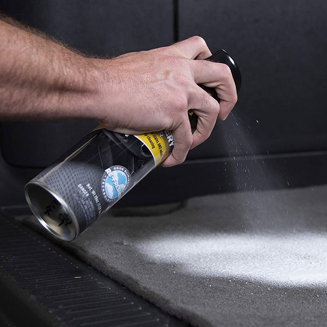 hand spraying Meguiars Carpet And Upholstery Cleaner on the carpet in a car