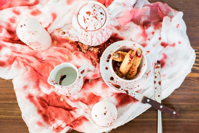 Bloody Halloween composition: high angle view of ceramic crockery in blood placed on dirty gauze, witch finger cookies in bloody cup