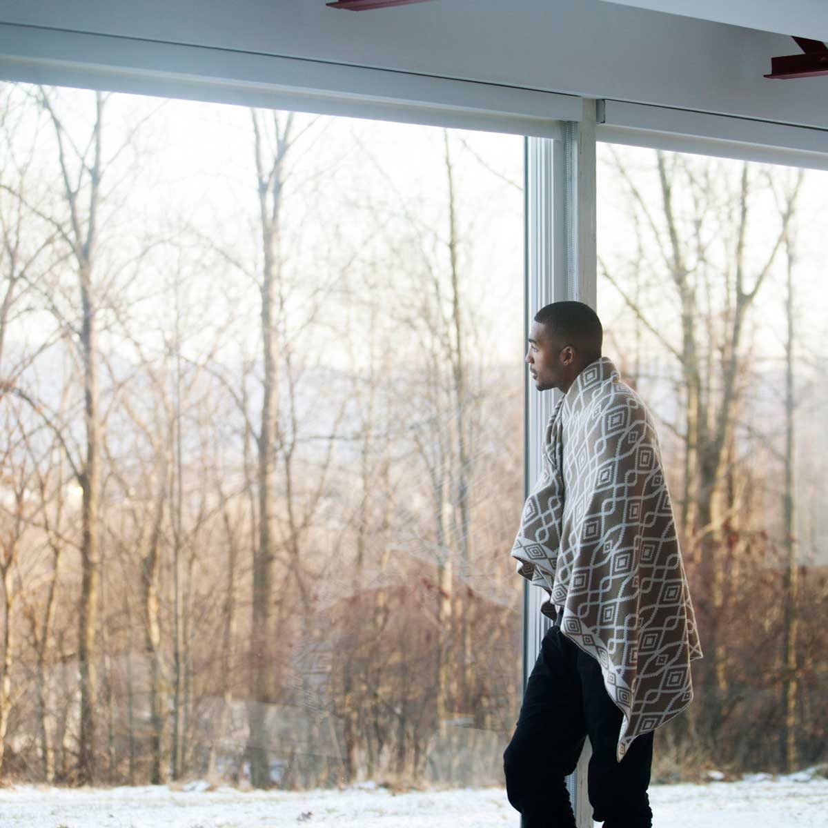 Man wearing a blanket by a window