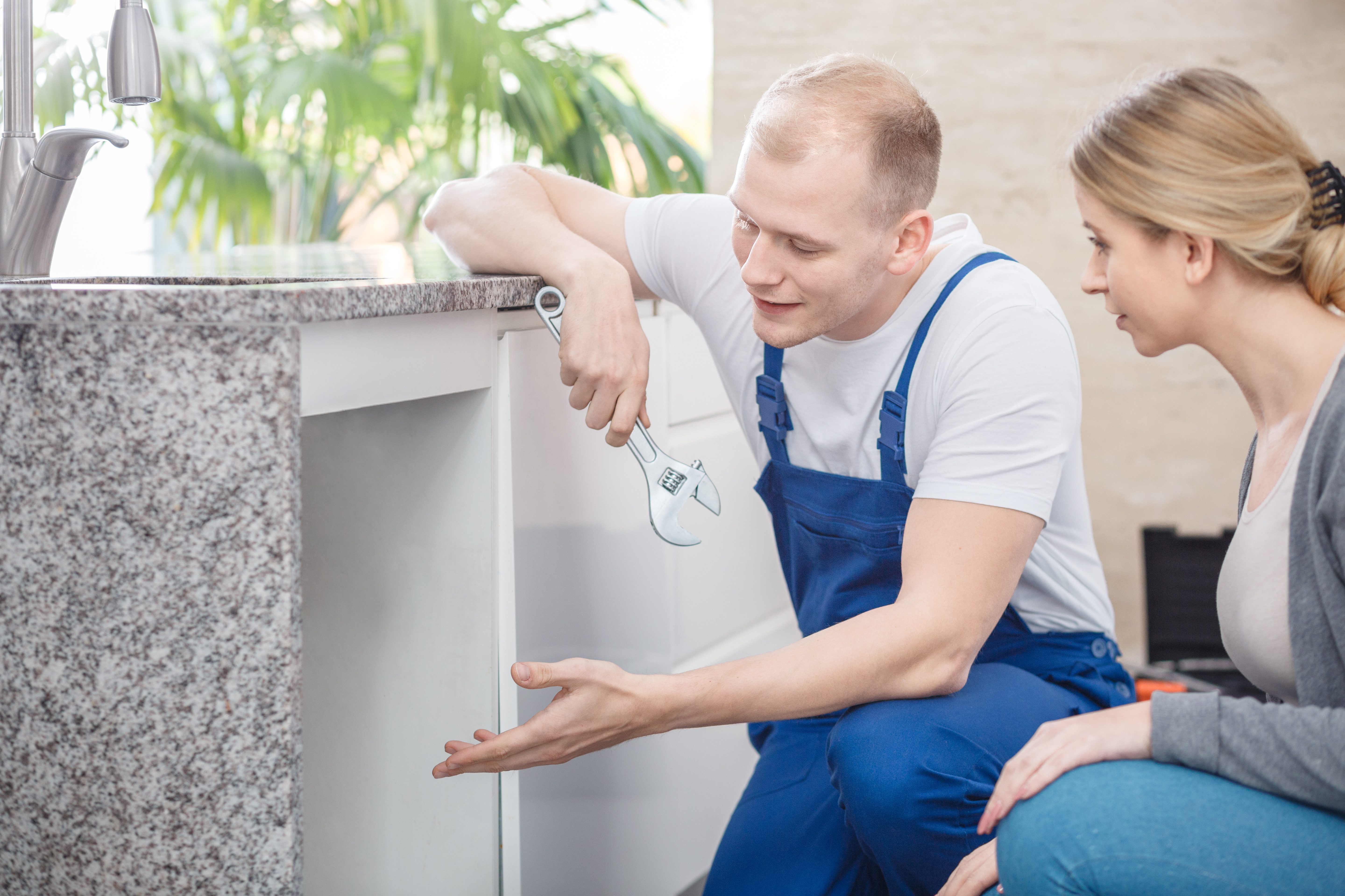 Plumber holding a wrench talking with a housewife about faucet damage