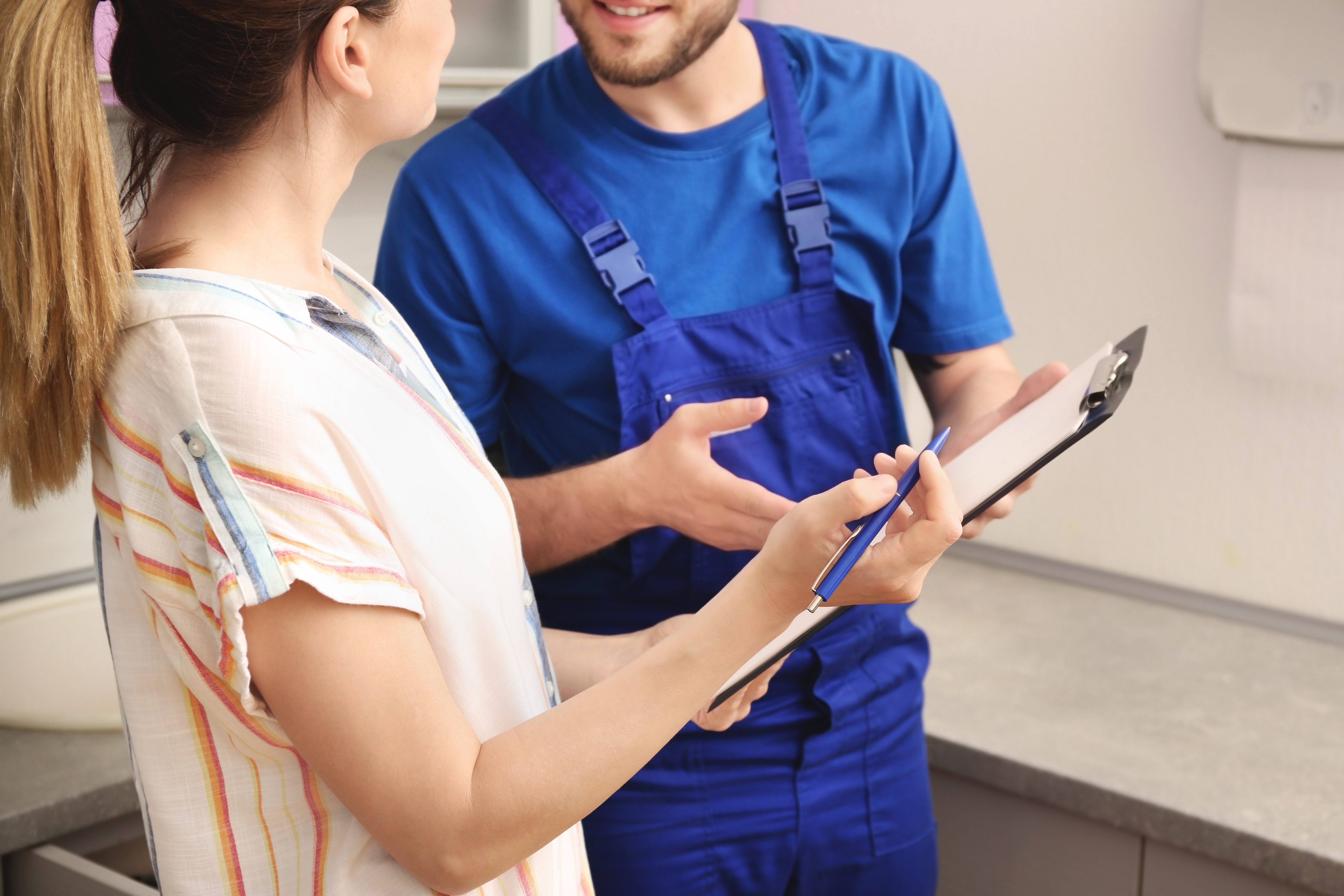 Professional plumber in uniform talking to client indoors