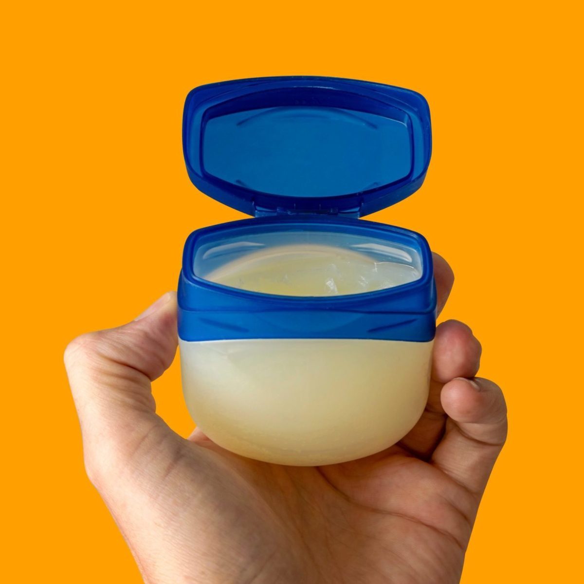 The left hand of a young female person holds a container with skincare cream over colored clean background.