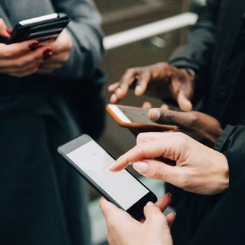 Midsection Of Colleagues Using Mobile Phones While Standing On Road In City