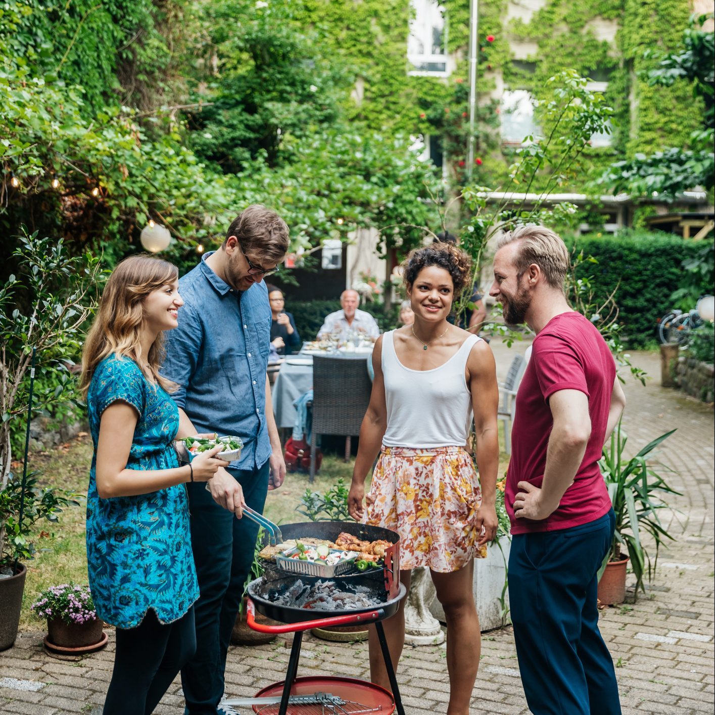 Group Of Friends Cooking On BBQ In Courtyard