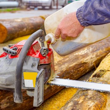 Carpenter pours motor oil from a plastic bottle into a chainsaw