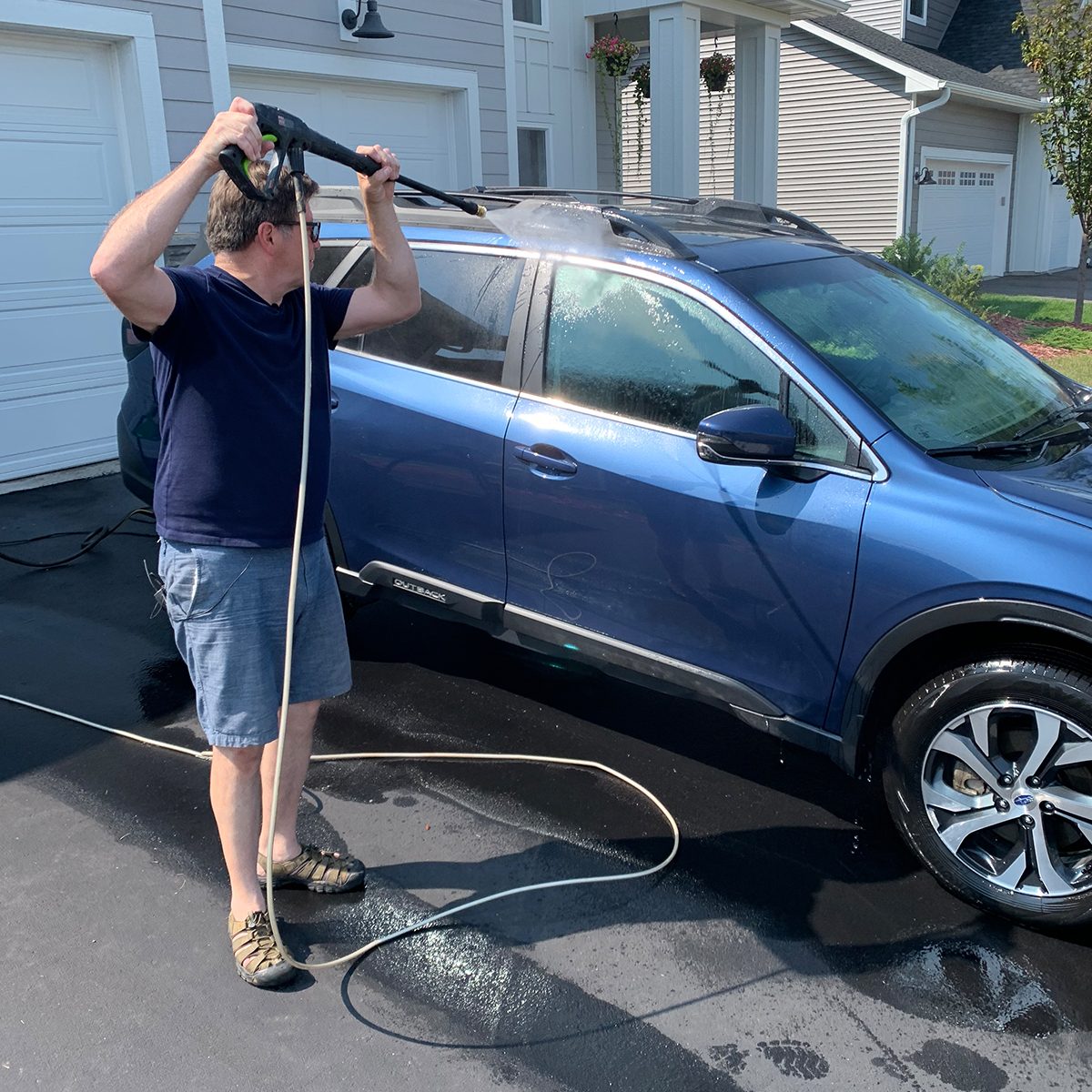 man pressure washing his car in driveway