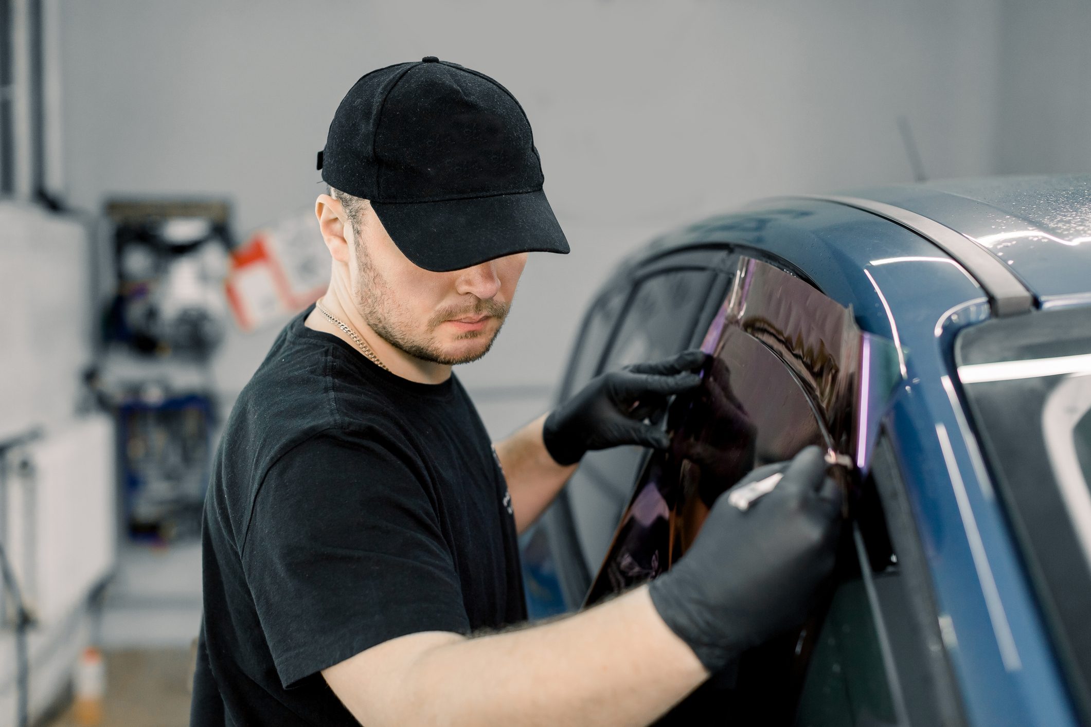 man applying window tint to car window in the shop