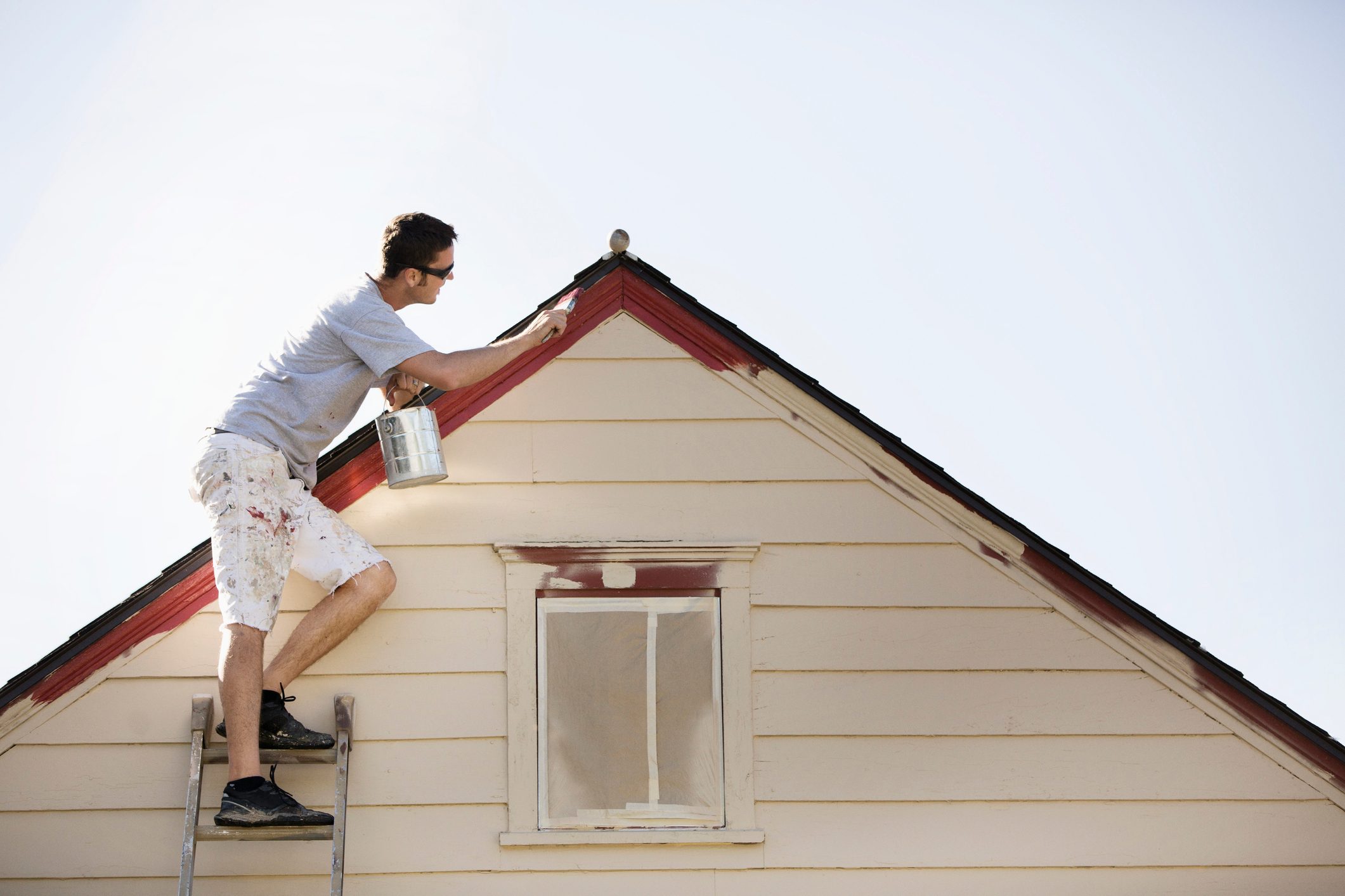 young man on a ladder painting edge of roof