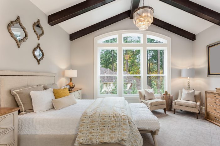 Master Bedroom In New Luxury Home With Chandelier And Large Bank Of Windows With View Of Trees