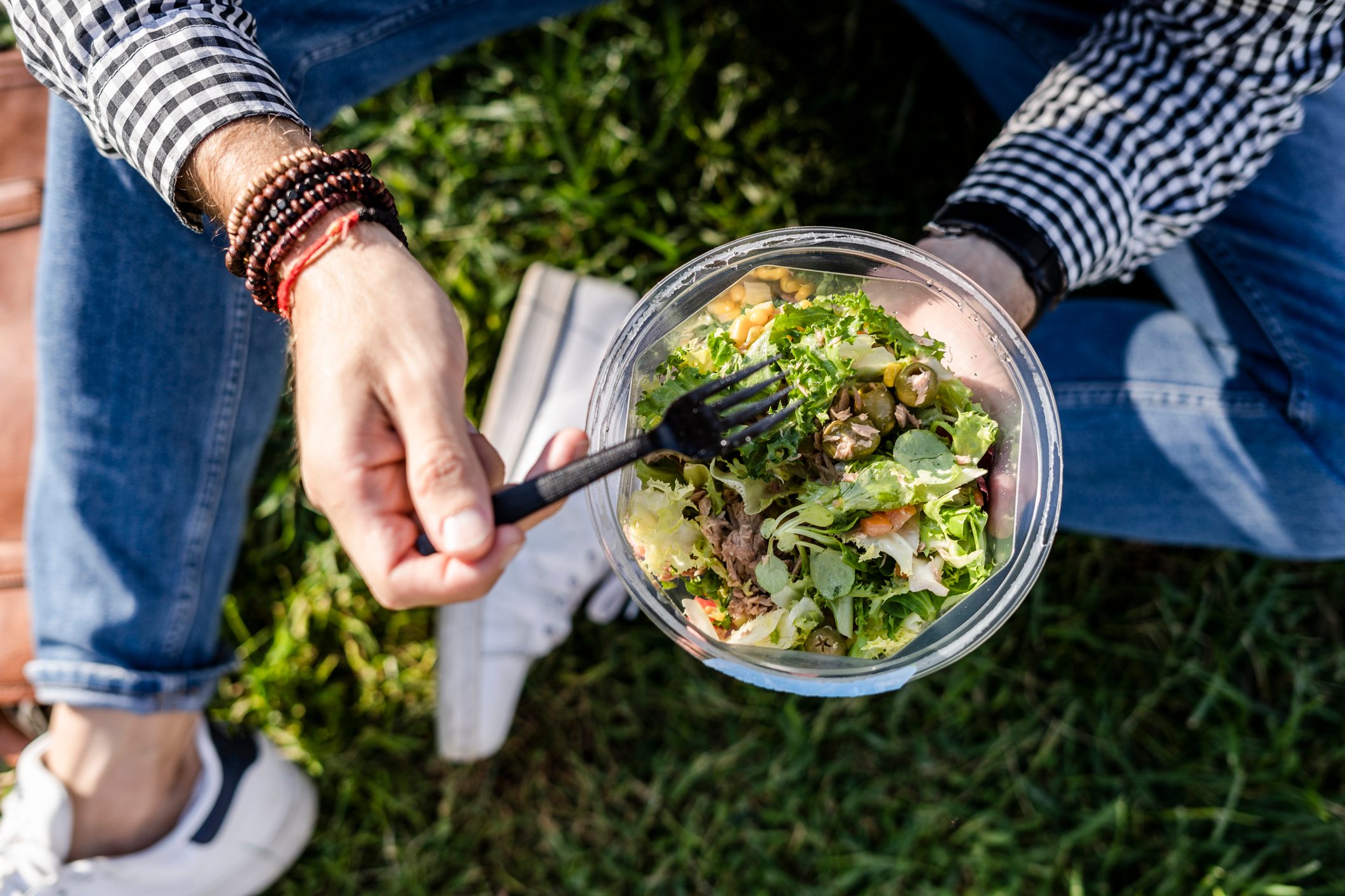 Man sitting on a meadow eating mixed salad, partial view