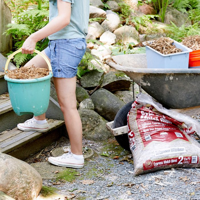 in a garden setting, wheelbarrow full of smaller buckets with mulch; person walking away with one of the smaller buckets
