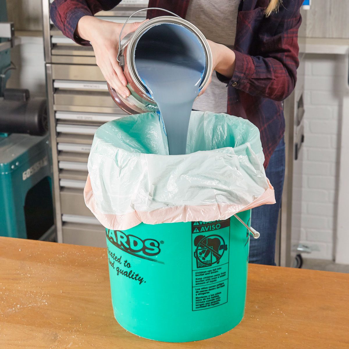 person pouring paint into a 5 gallon bucket that is lined with a garbage bag