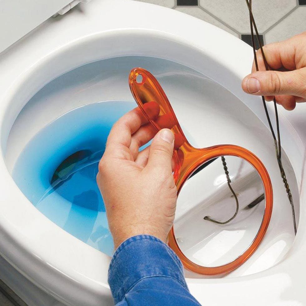 close up of a hand holding an orange mirror and a hanger to fix a toilet