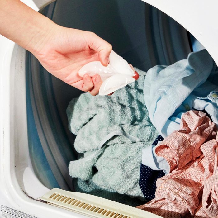 close up of hand putting an ice cube into a dryer with clothes