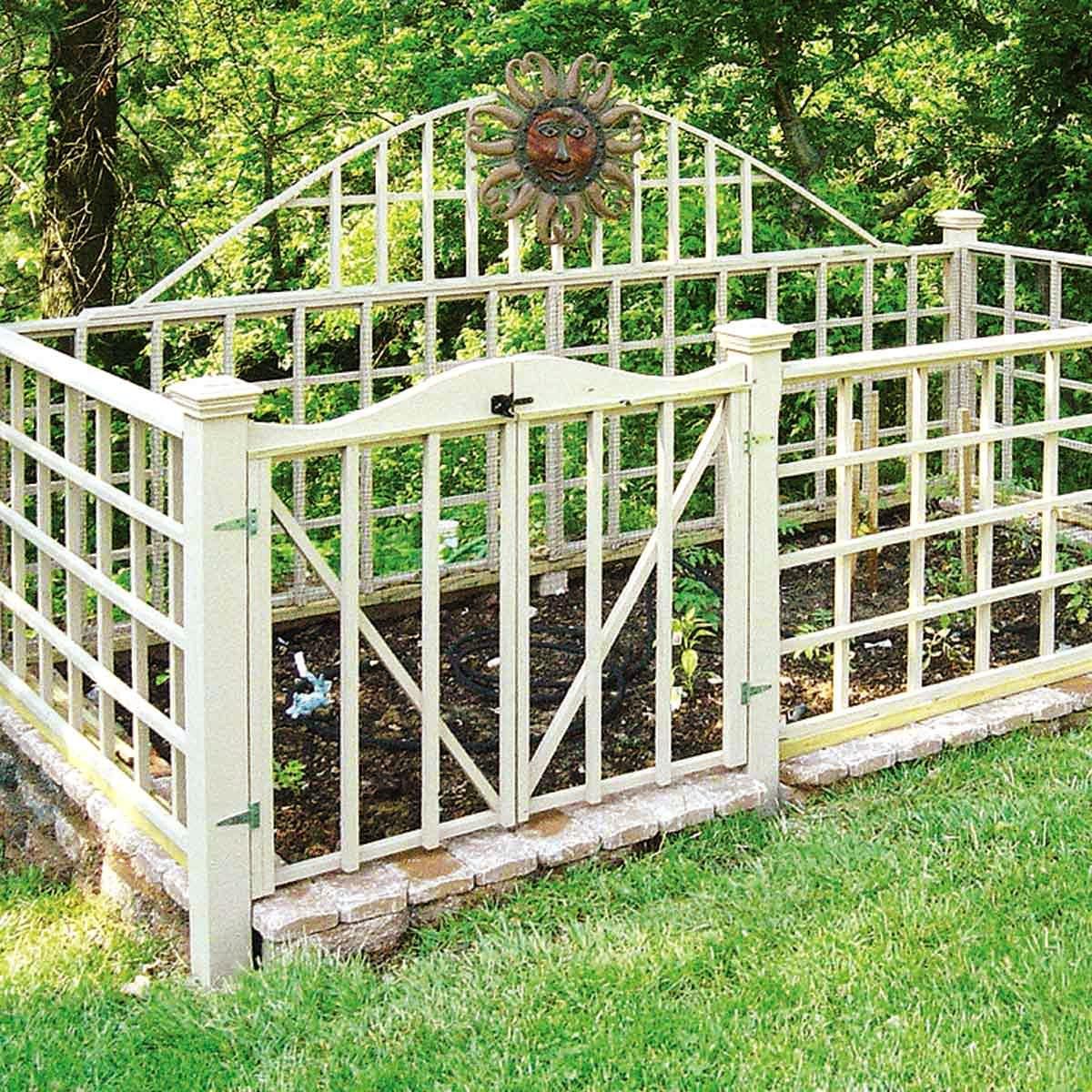 small dirt garden surrounded by a white wooden fence with a sun hanging towards the back