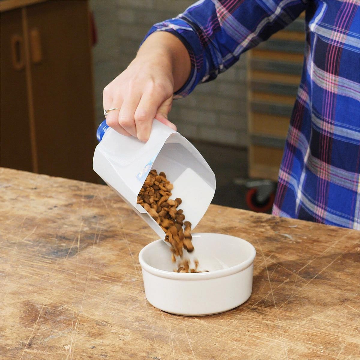 close up of hand using a milk jug as a scoop to poor dog food into a bowl