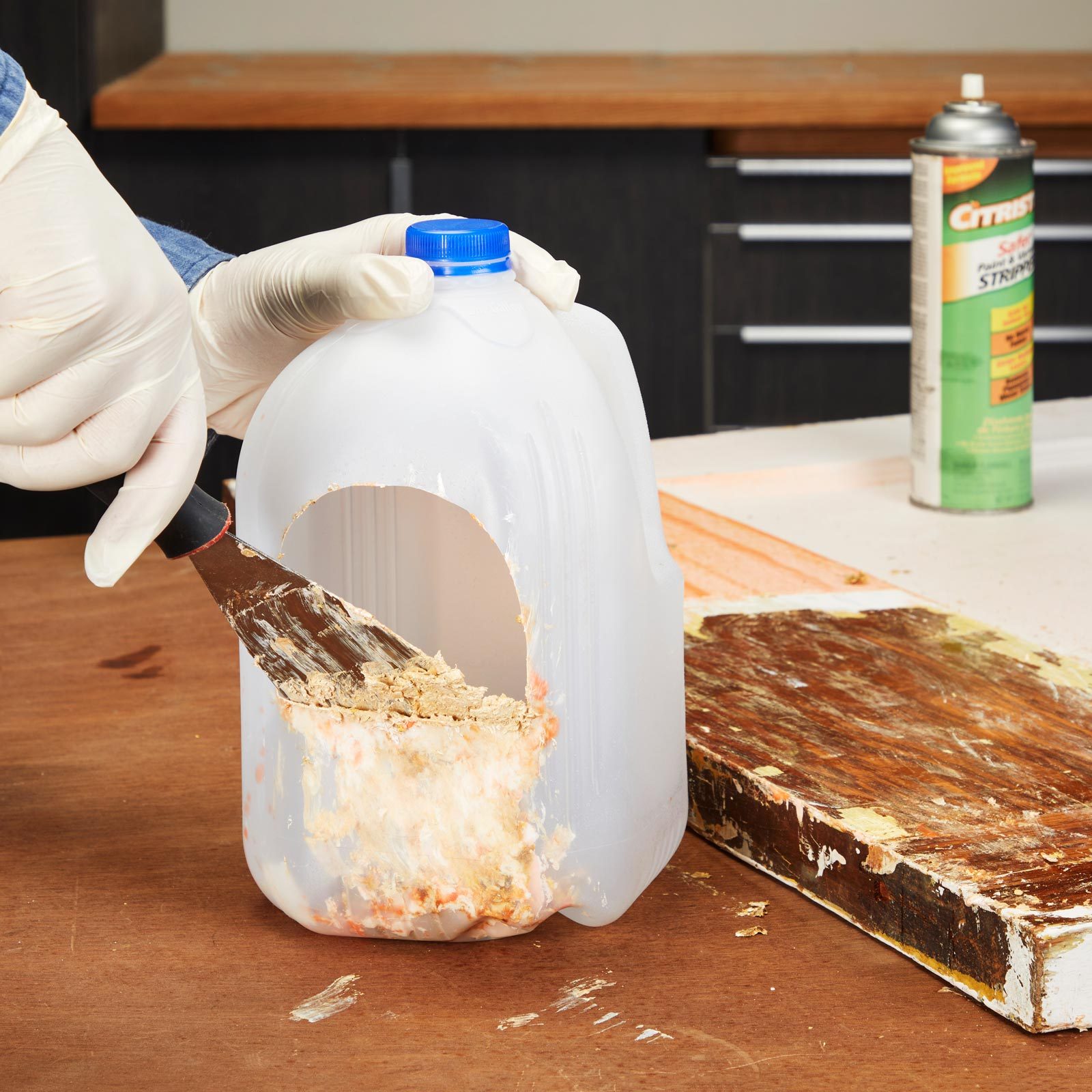 gloved hand scrapping a pudy knife on a milk jug with a whole cut in the side