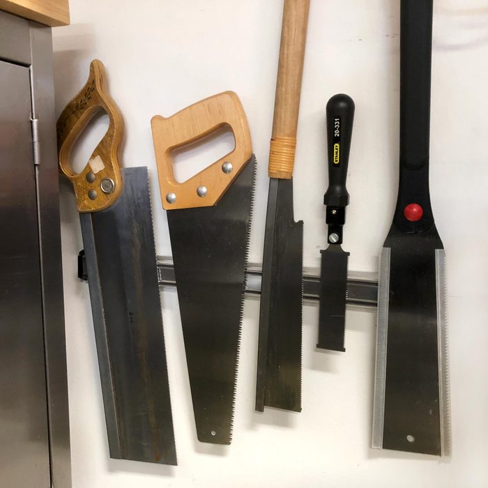 a magnetic strip of sheet metal with a variety of saws and tools hanging from it