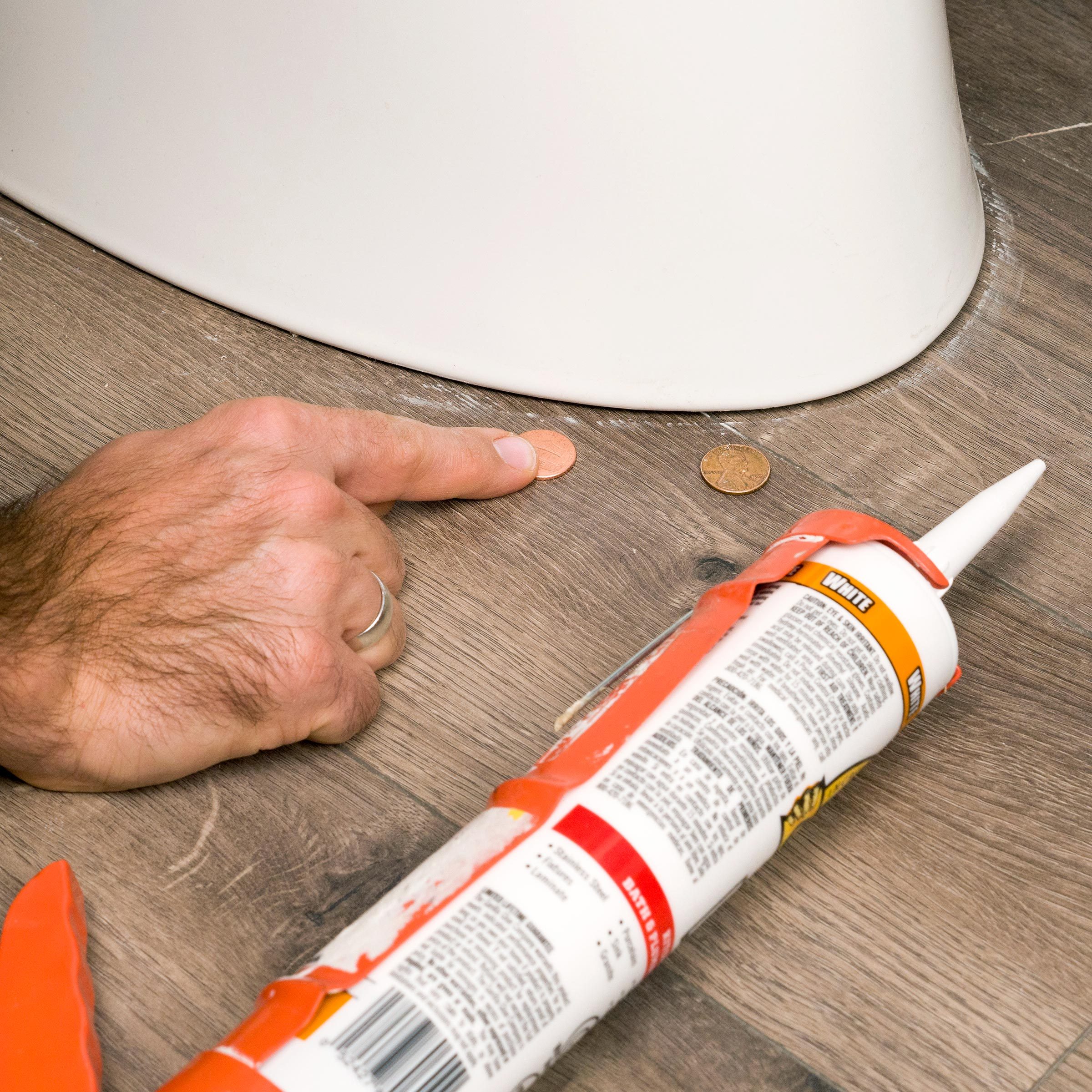 hand pointing to pennies next to a Toilet and a tube of caulk