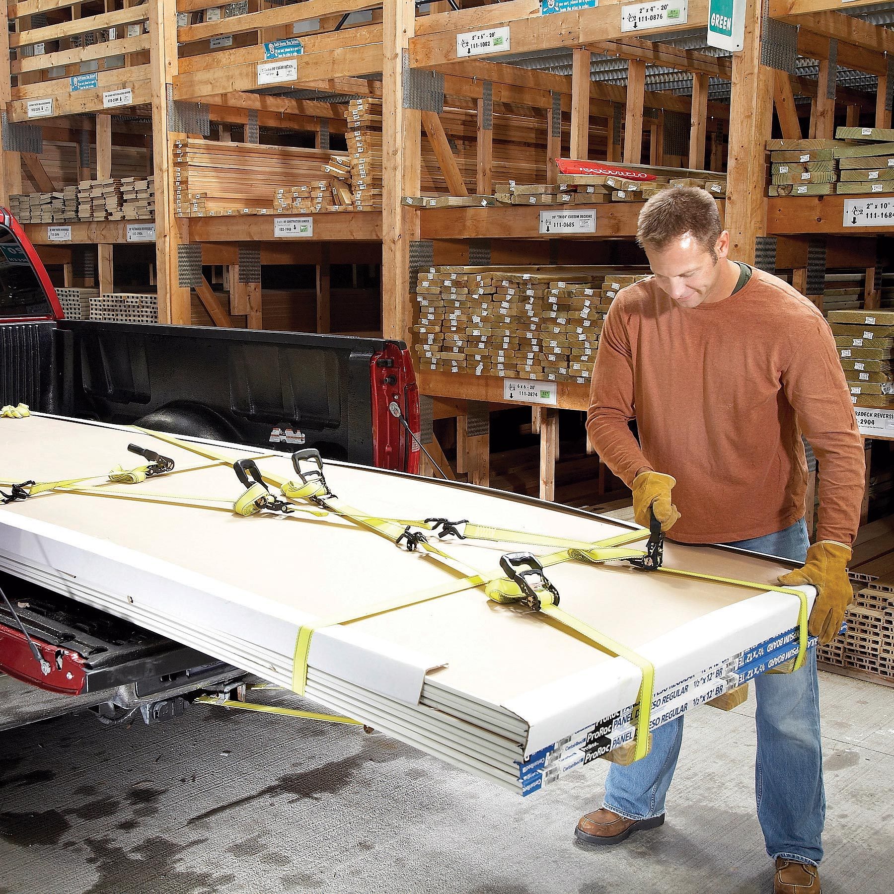 man strapping in long pieces of lumber into a pick up truck