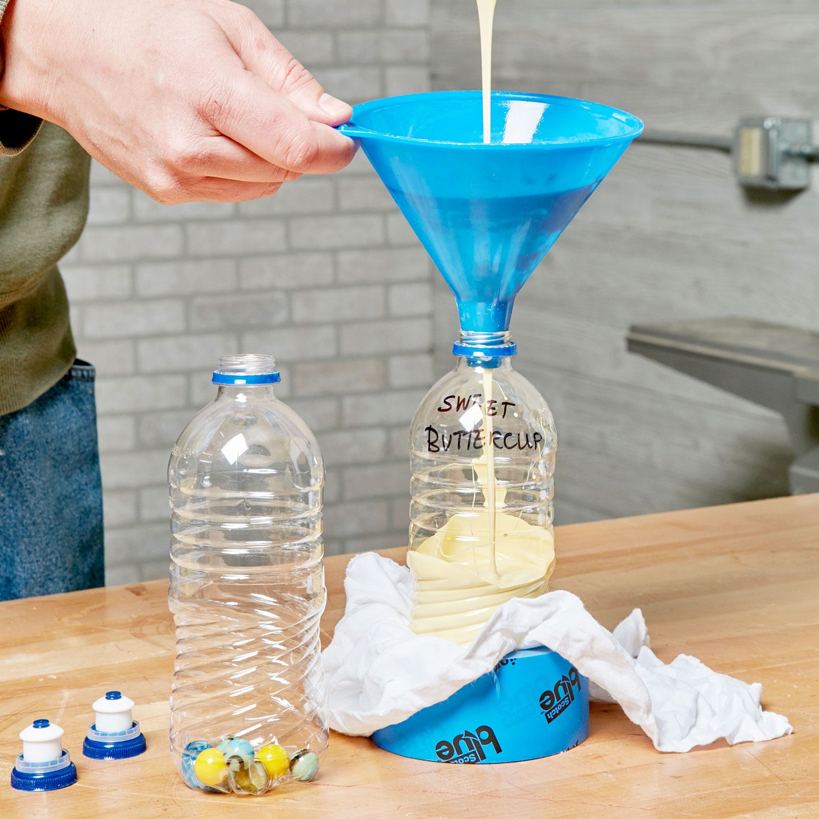 pouring paint into an empty water bottle with marbles in the bottom