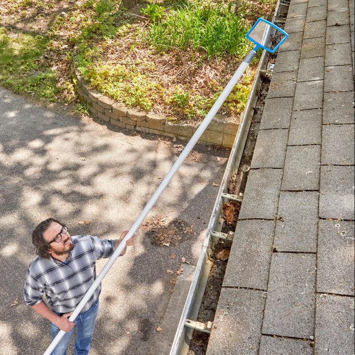 man checking gutters from the ground using a long pole with a mirror at the end