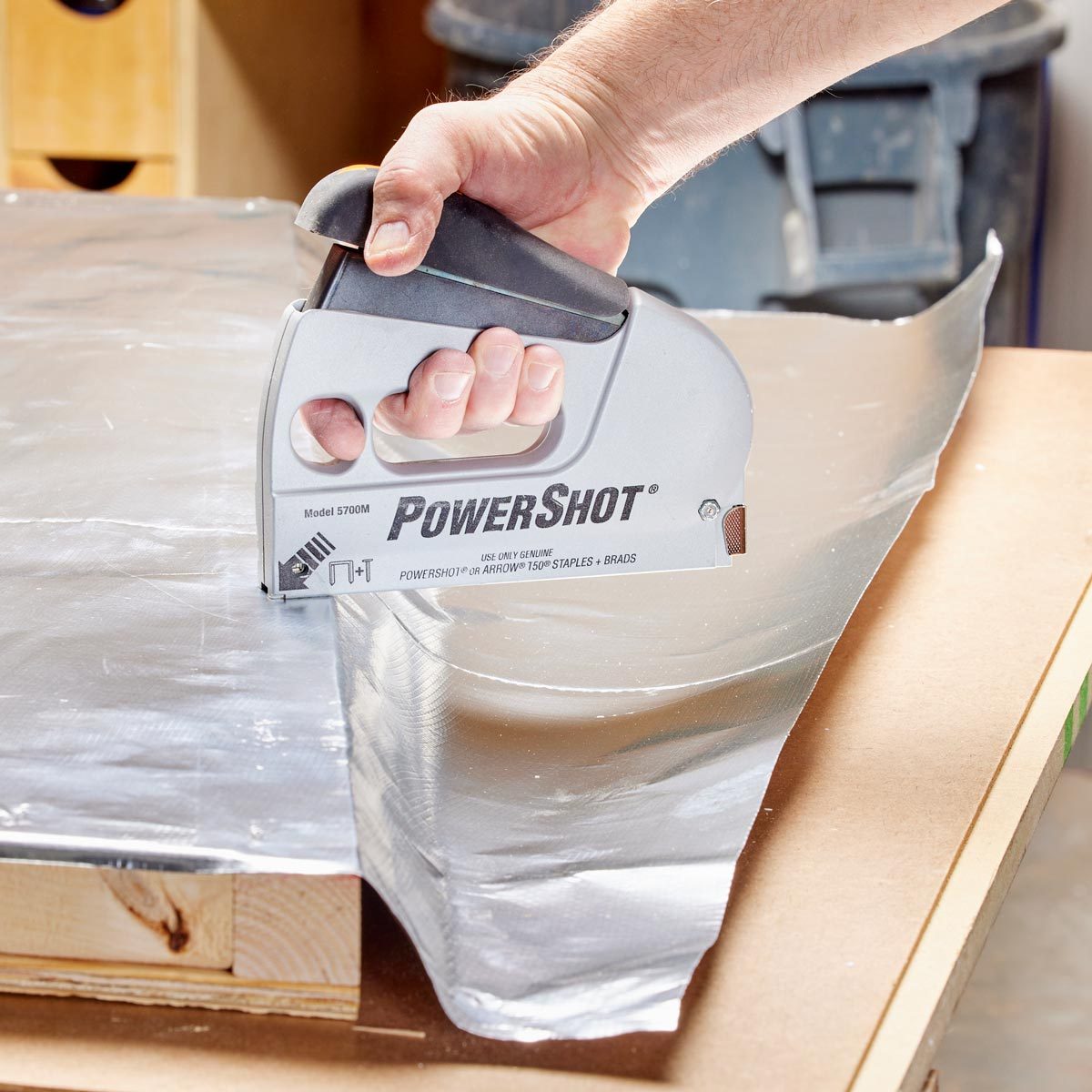 close up of a hand using a staple gun to attach foil vapor barrier to the interior of the sauna wall