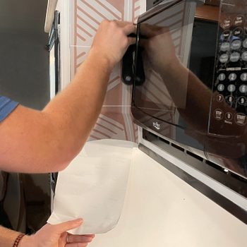 close up of hands applying peel and stick tile wallpaper in a kitchen wall as a backsplash