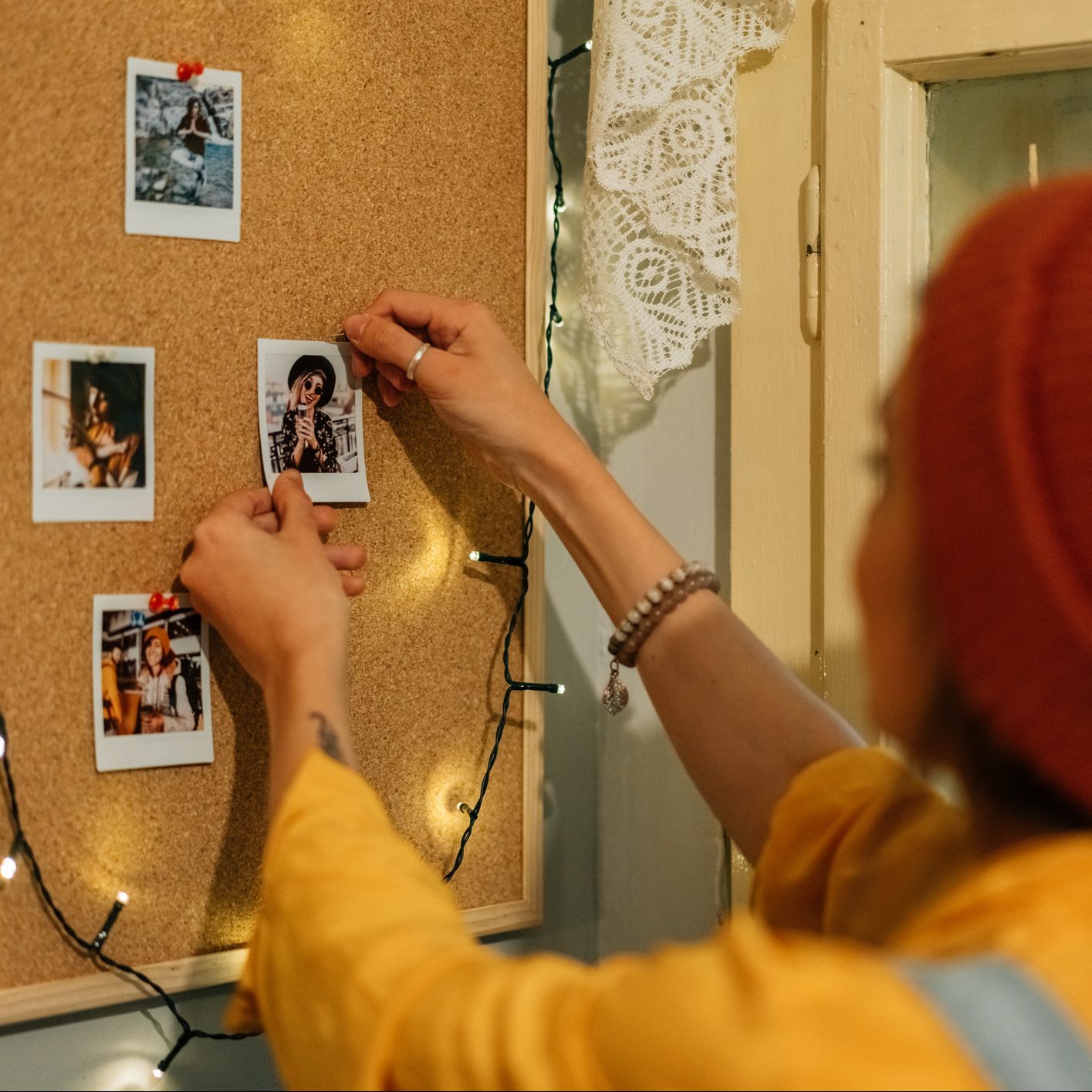 Girl creating collection of instant photo memories on bulletin board for college dorm room