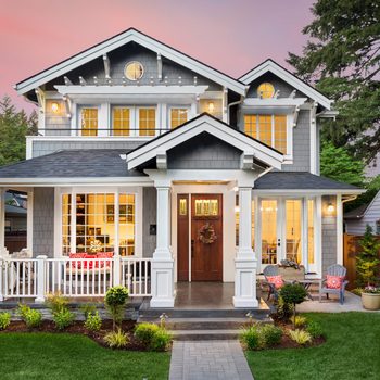 Beautiful pewter colored luxury home exterior with glowing interior lights at sunset in suburban neighborhood