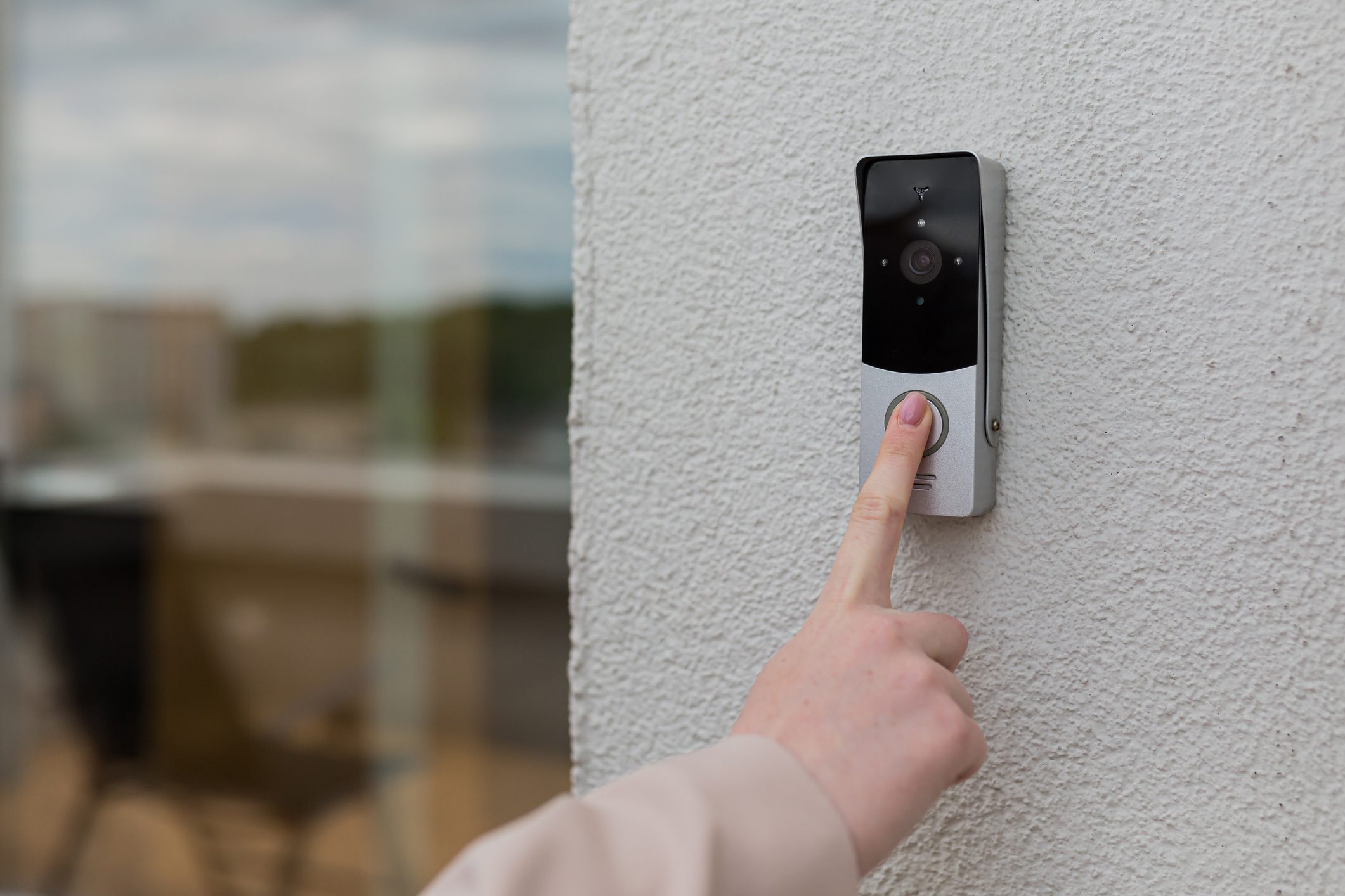 woman's hand uses a doorbell on the wall of the house with a surveillance camera